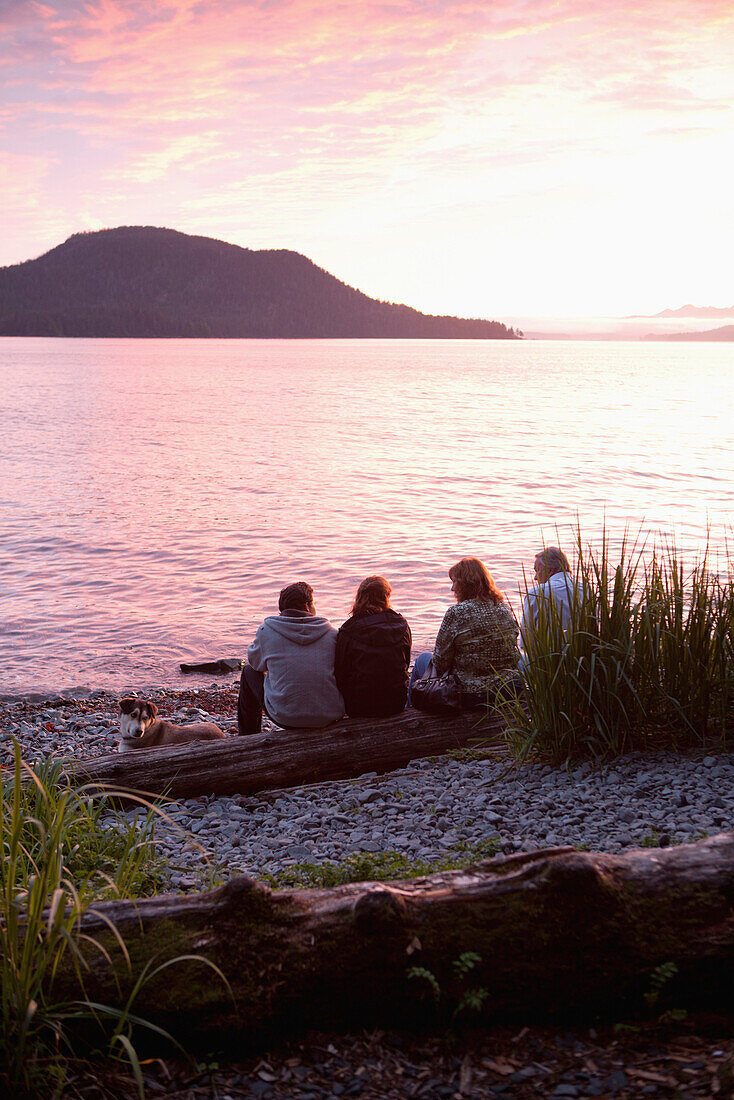 ALASKA, Sitka, people enjoy the sunset and sit on a log at Halibut Cove, Sitka Sound