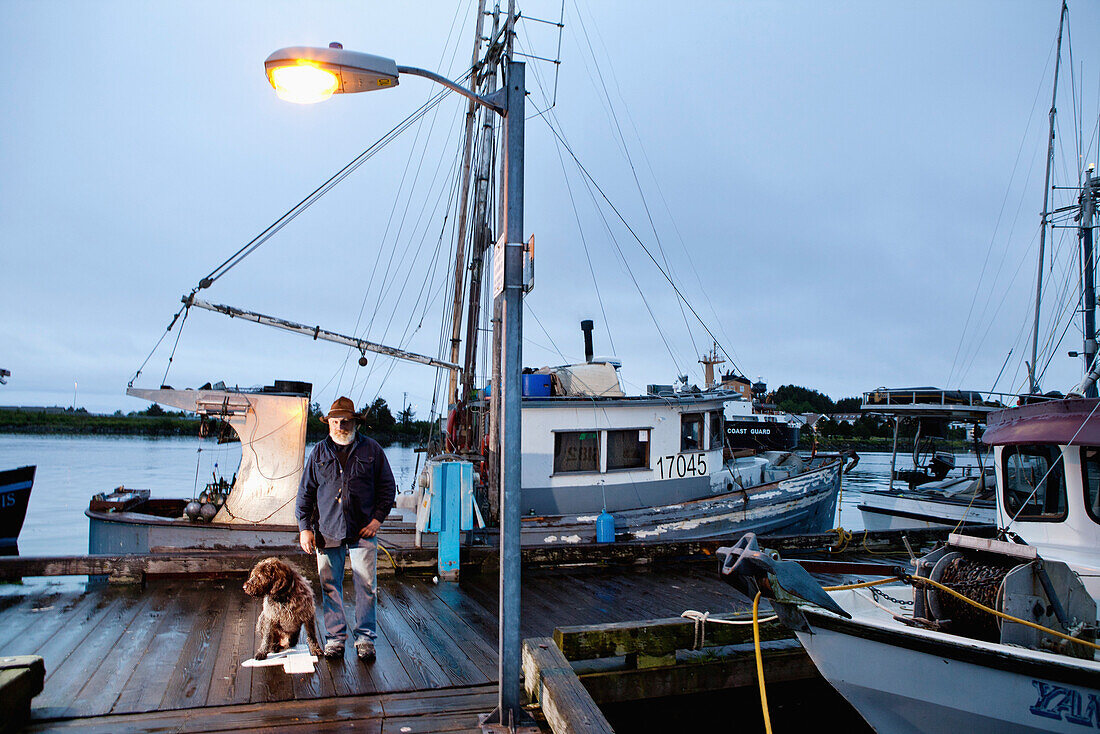 ALASKA, Sitka, fisherman Bill Dorn and his dog Baranof on the dock by an old fishing boat in the Sitka Harbor
