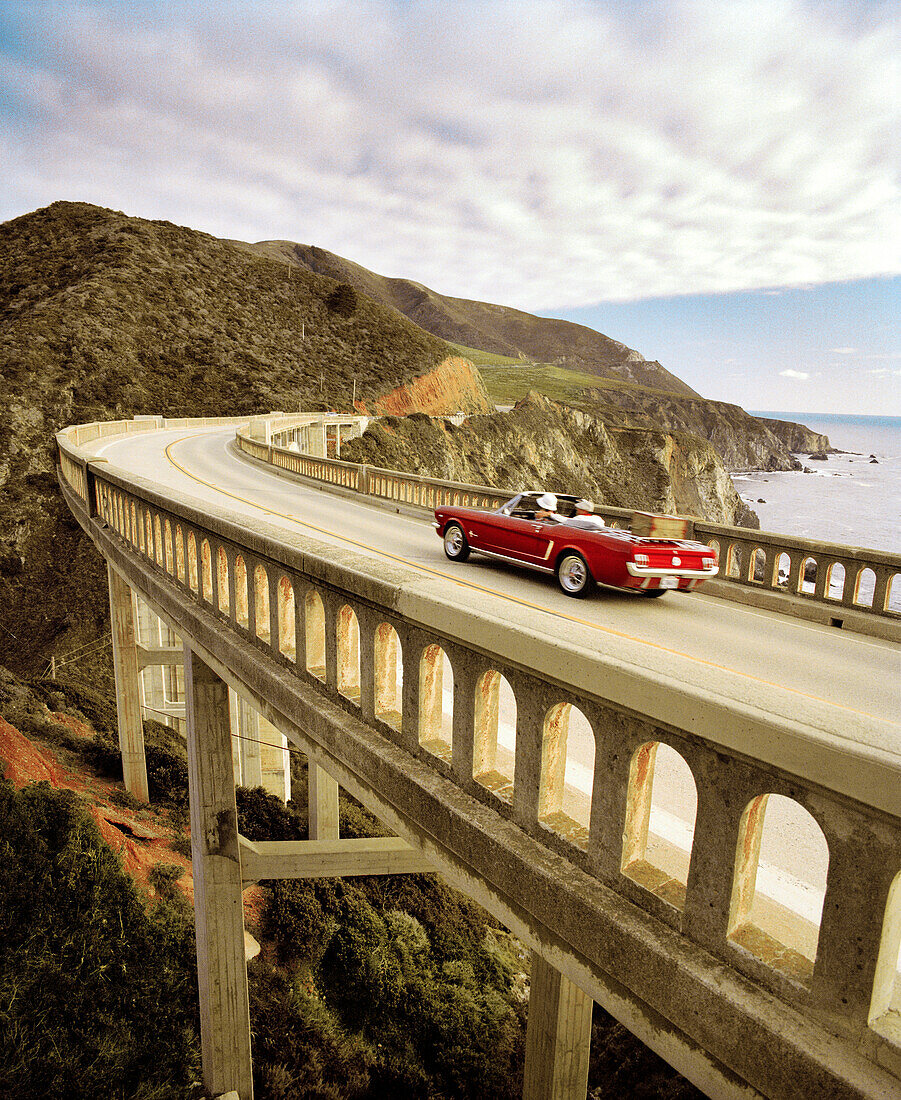 USA, California, Big Sur, couple in a 1965 Mustang on a road trip, Bixby Bridge, Hwy 1