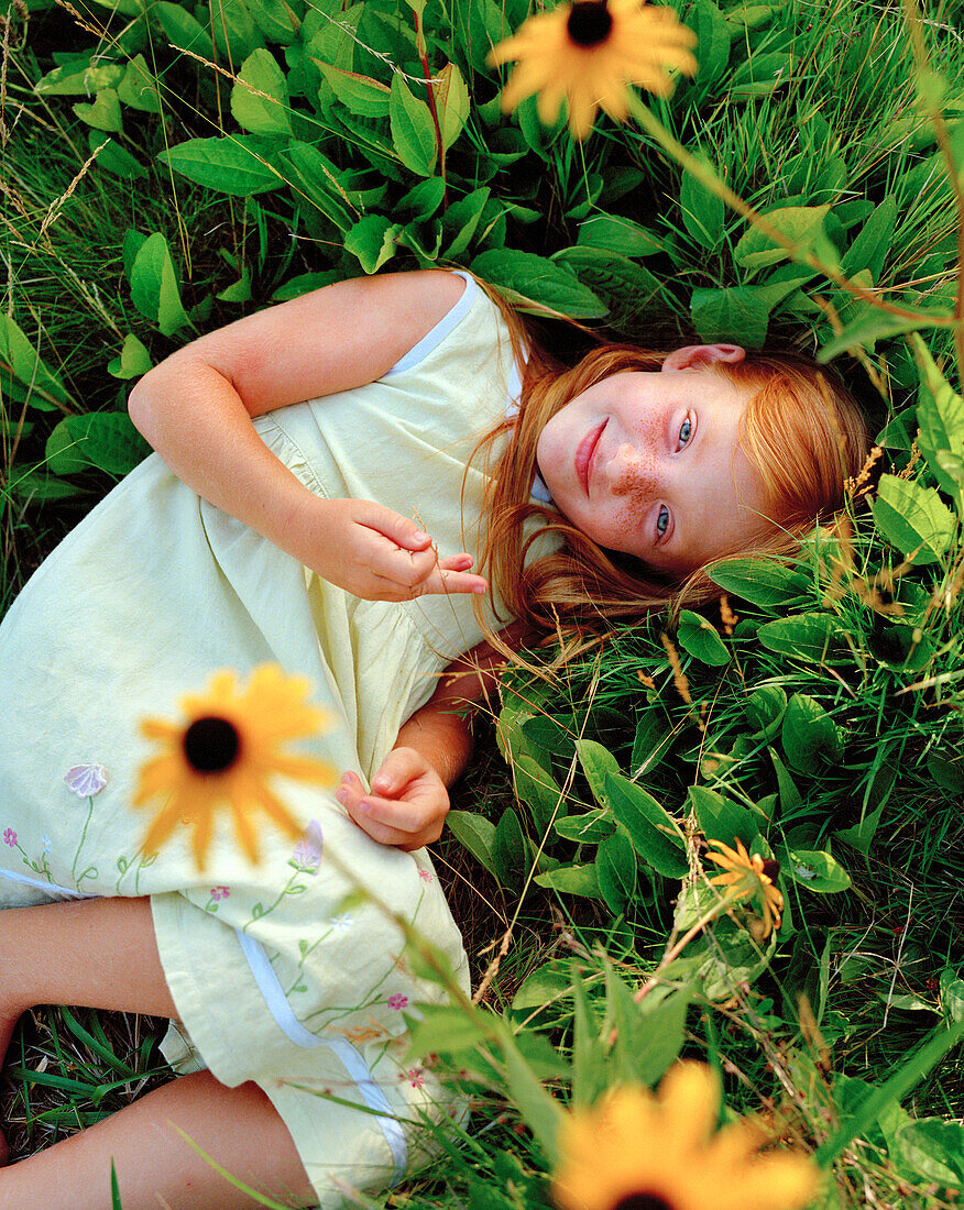 USA, California, portrait of smiling girl lying in the grass and flowers