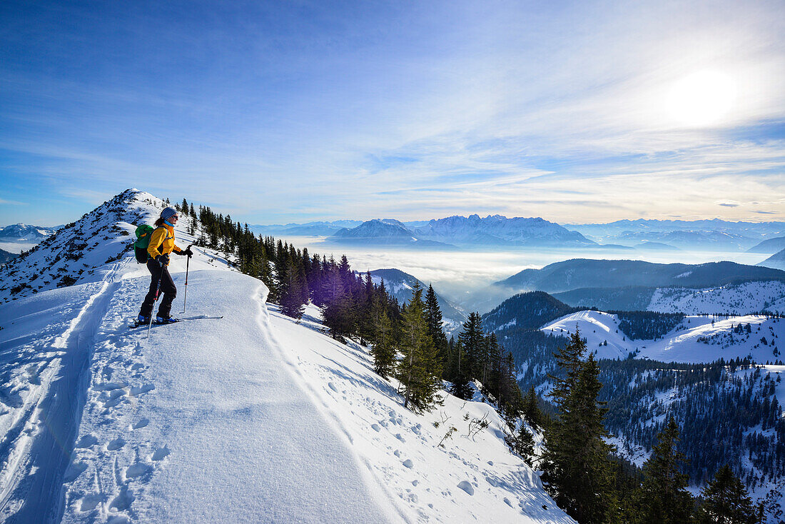 Female back-country skier ascending to Grosser Traithen, Kaiser mountain range in background, Mangfall range, Bavarian Alps, Upper Bavaria, Bavaria, Germany