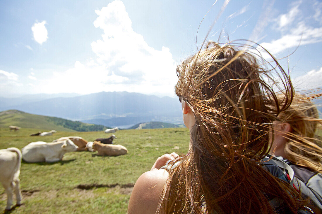Two young women looking at a herd of cows, Alpe-Adria-Trail, Nockberge, Carinthia, Austria