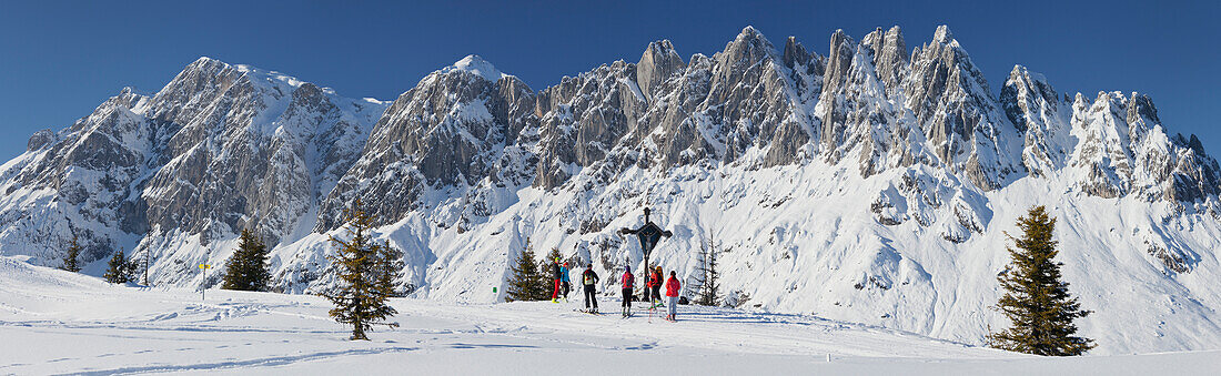 View from Hochkeil to Hochkoenig in Winter, Summit cross with cross country skiers, Muehlbach, Salzburg Land, Austria