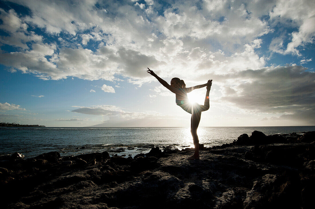 Woman practicing yoga on rock formation. Kapalua Bay