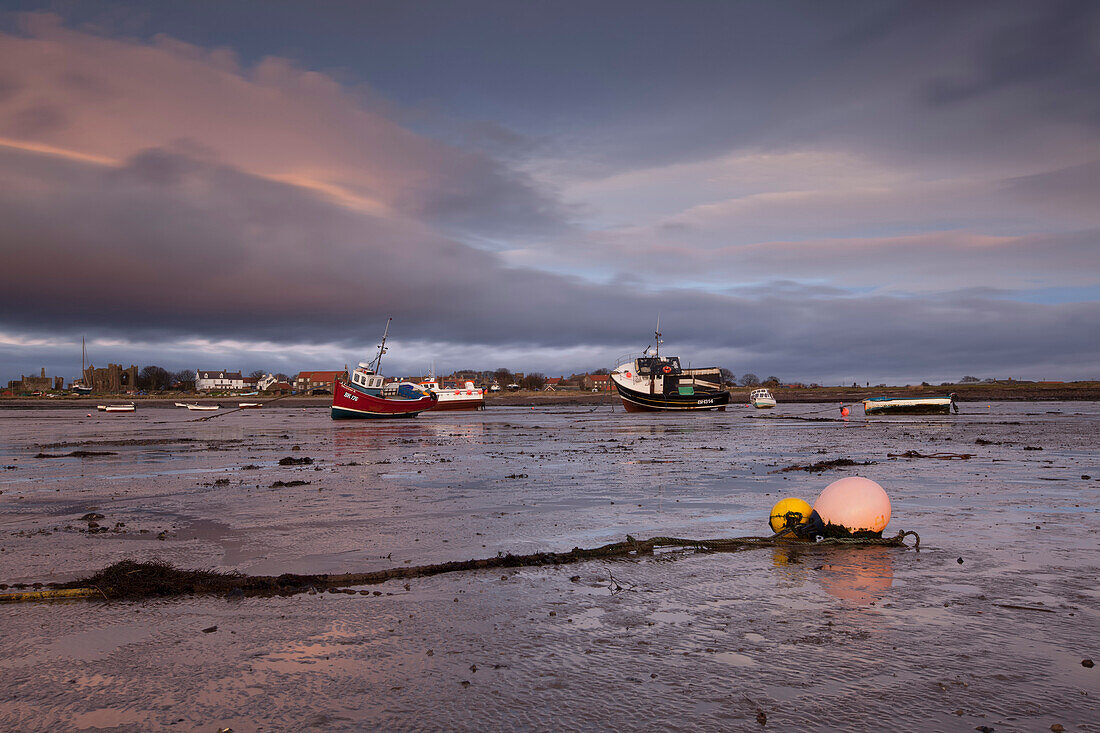 Sonnenaufgang über dem Hafen von Lindisfarne mit auf dem Watt liegenden Booten bei Ebbe, Lindisfarne, Holy Island, Northumberland, England, Großbritannien