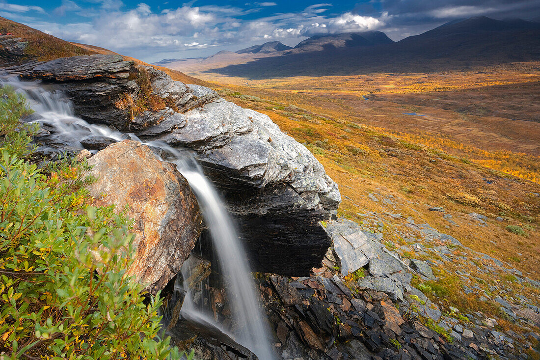 Blick über den Abisko Nationalpark mit Wasserfall im Vordergrund und Lapporten im Hintergrund im Herbst, Lappland, Schweden