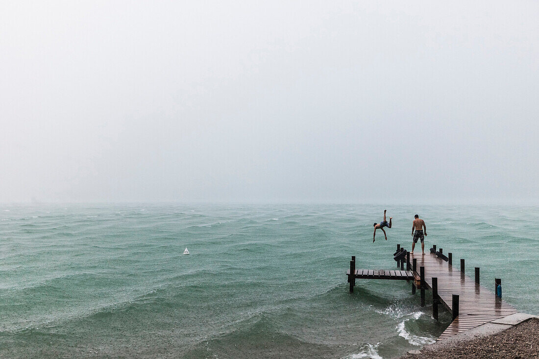 Two young men on a jetty at Lake Starnberg in rain, Bavaria, Germany