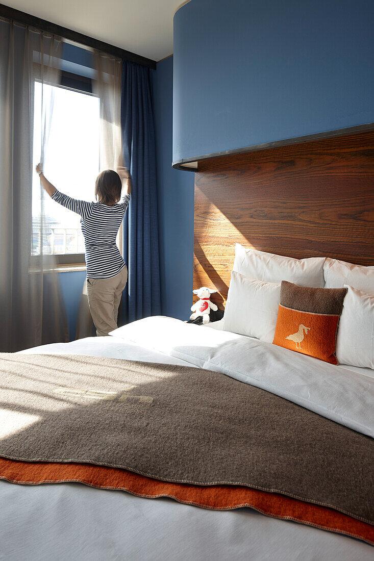 Woman at the window of a 'M plus berth' room with harbour view, 25hours Hotel, HafenCity, Hamburg, Germany