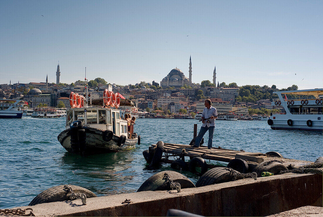 Republic of Turkey, Istanbul, The edge of the Golden Horn, The Süleymaniye Mosque, Man Fishing near a boat in a landing stage