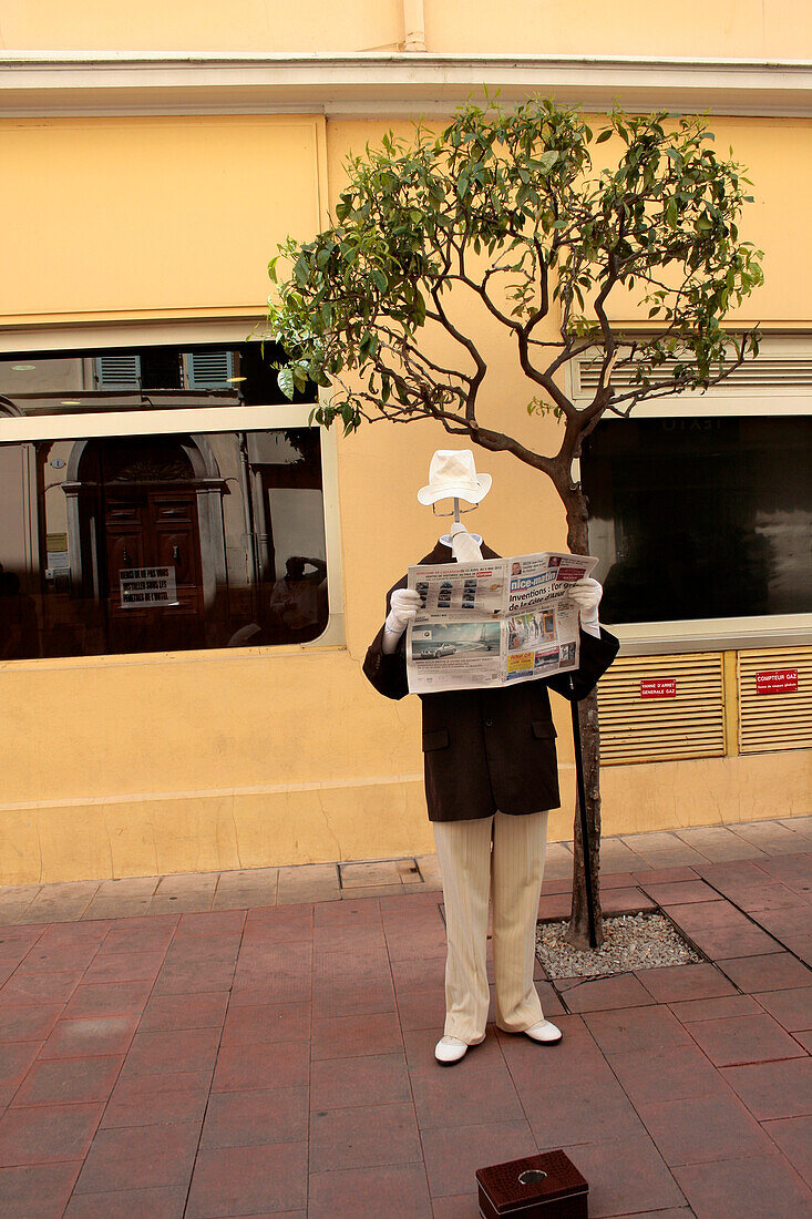 France, Provence - Alps- Côte d'Azur, Menton, Statue of a headless man reading a book, wearing a suit and a hat, in a pedestrian zone