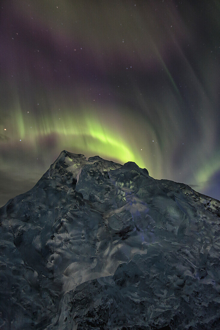 Aurora borealis dances over iceberg from the glacial lagoon jokulsarlon, iceland