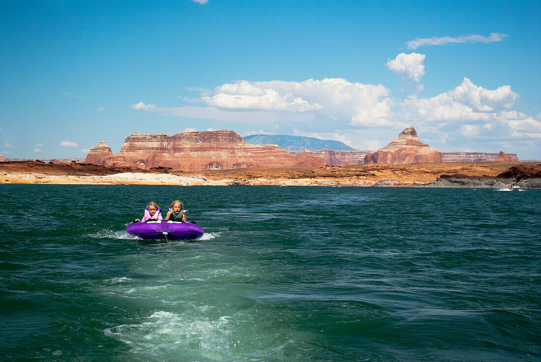 Mother and daughter ride on purple towable tube behind speedboat on lake powell, page arizona usa