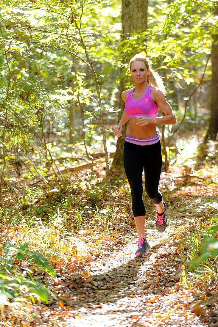 A 38 year old blond woman wearing work-out clothing jogging on a trail in a forest setting in the fall