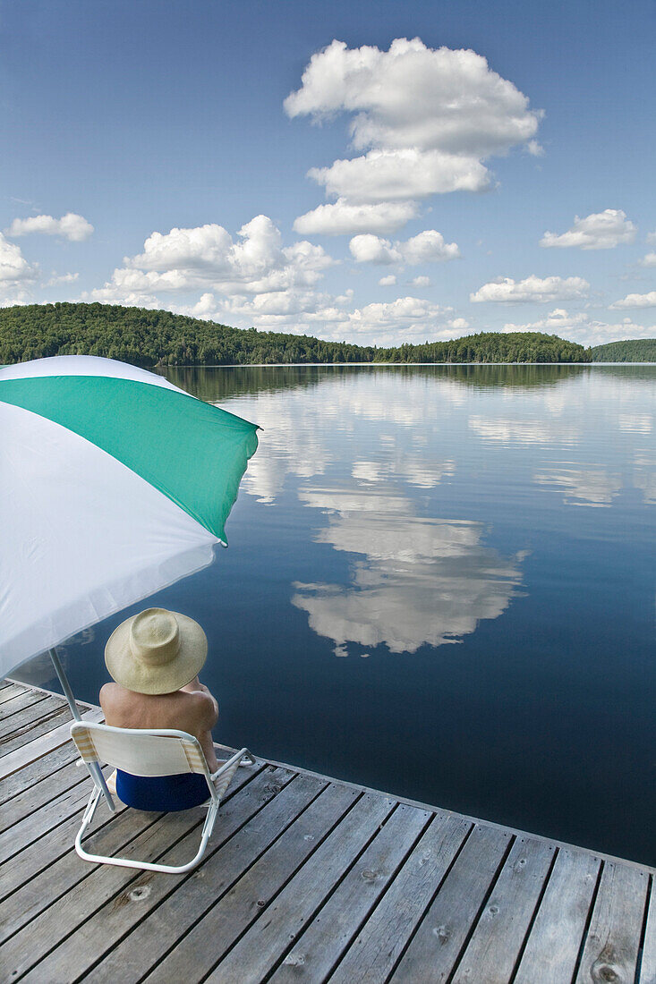 Woman sitting under umbrella on dock, Smoke Lake, Algonquin Park, Ontario