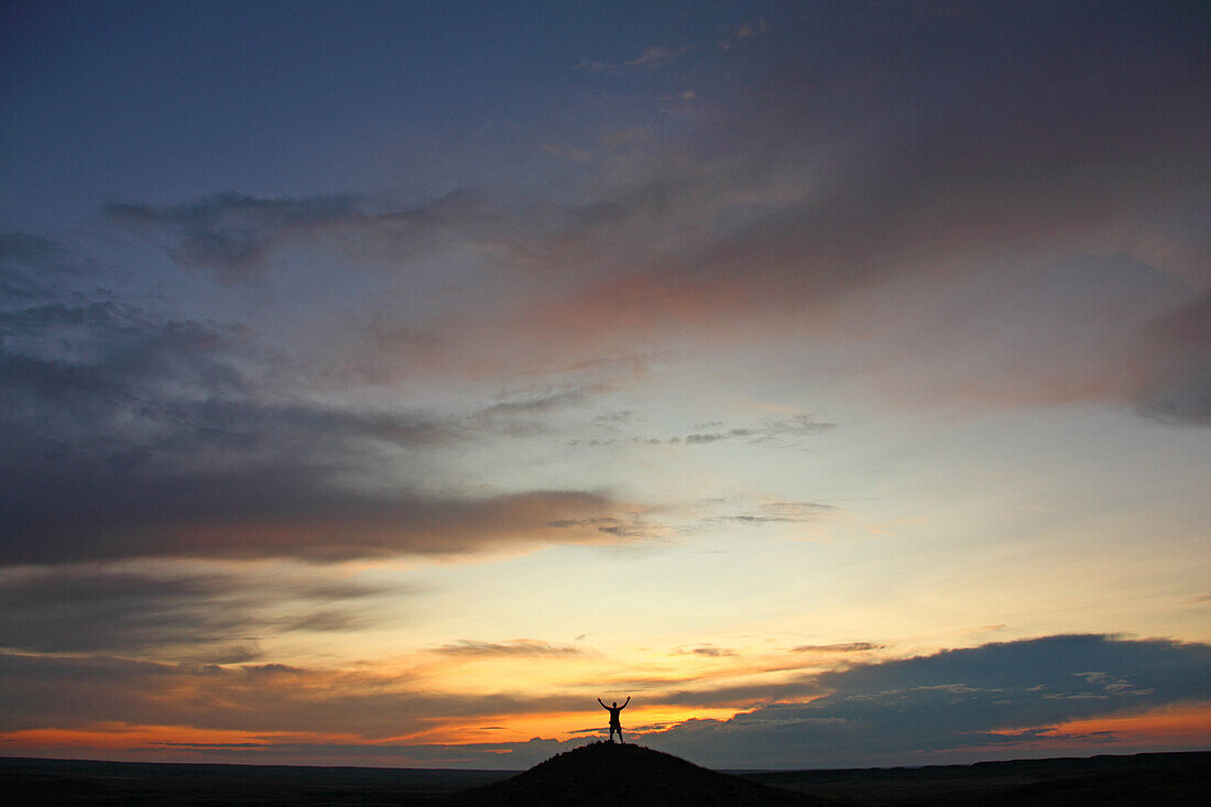 Man with arms outstretched on top of butte, at sunset, Grasslands National Park, Saskatchewan