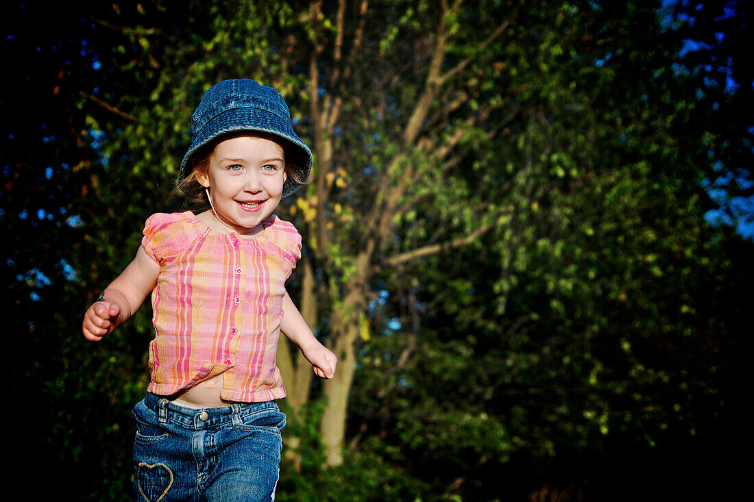 Young girl with blue denim hat running, Otterburn Park, Quebec