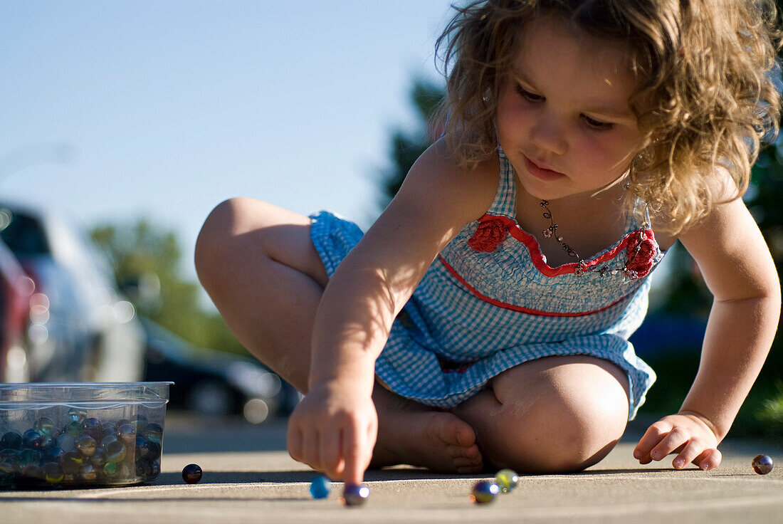 Young girl playing with marbles on sidewalk, Regina, Saskatchewan