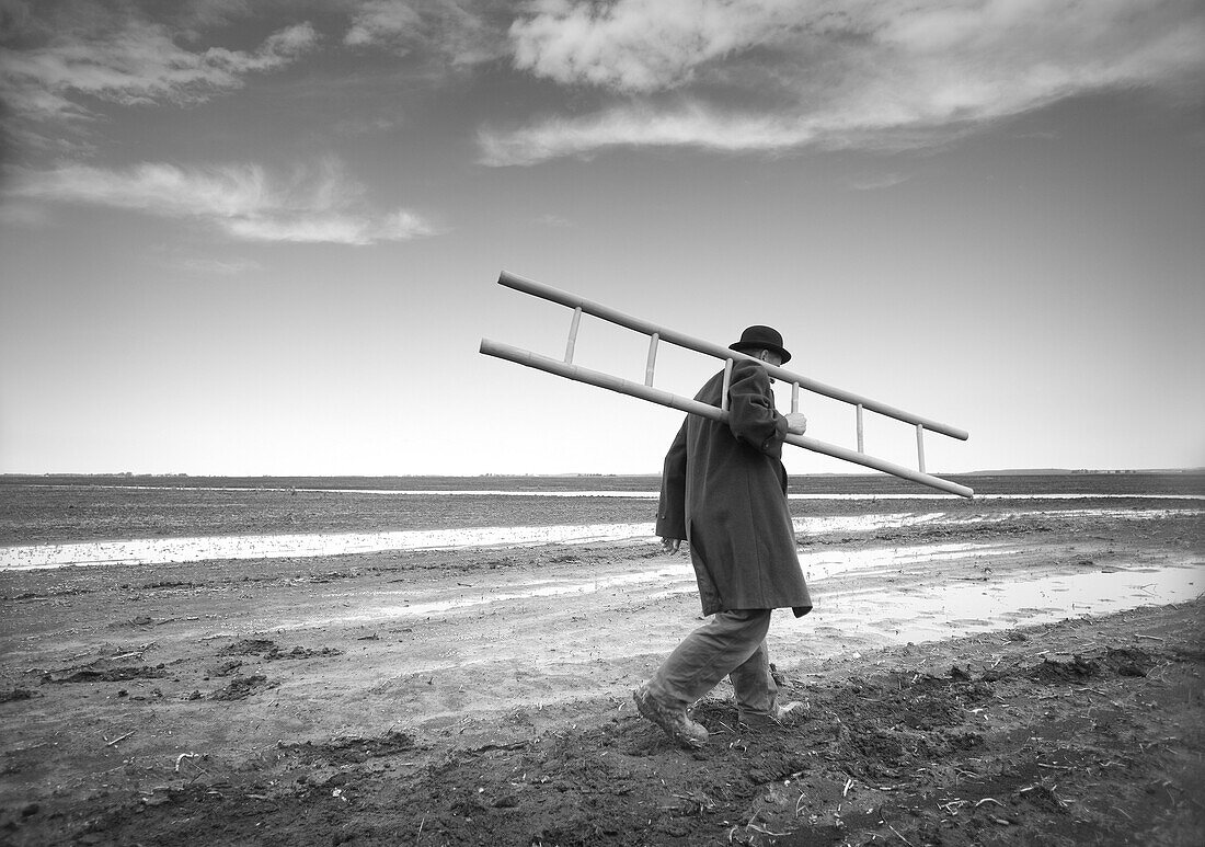 Man Carrying Ladder in Muddy Field, Winnipeg, Manitoba