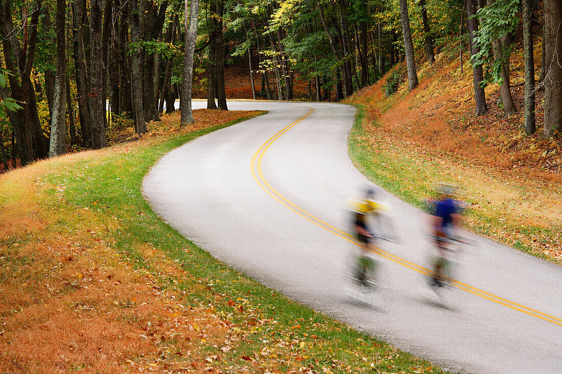 Man and woman cycling on a curvy road through mountain landscape in autumn, Blue Ridge Parkway National Park, Virginia