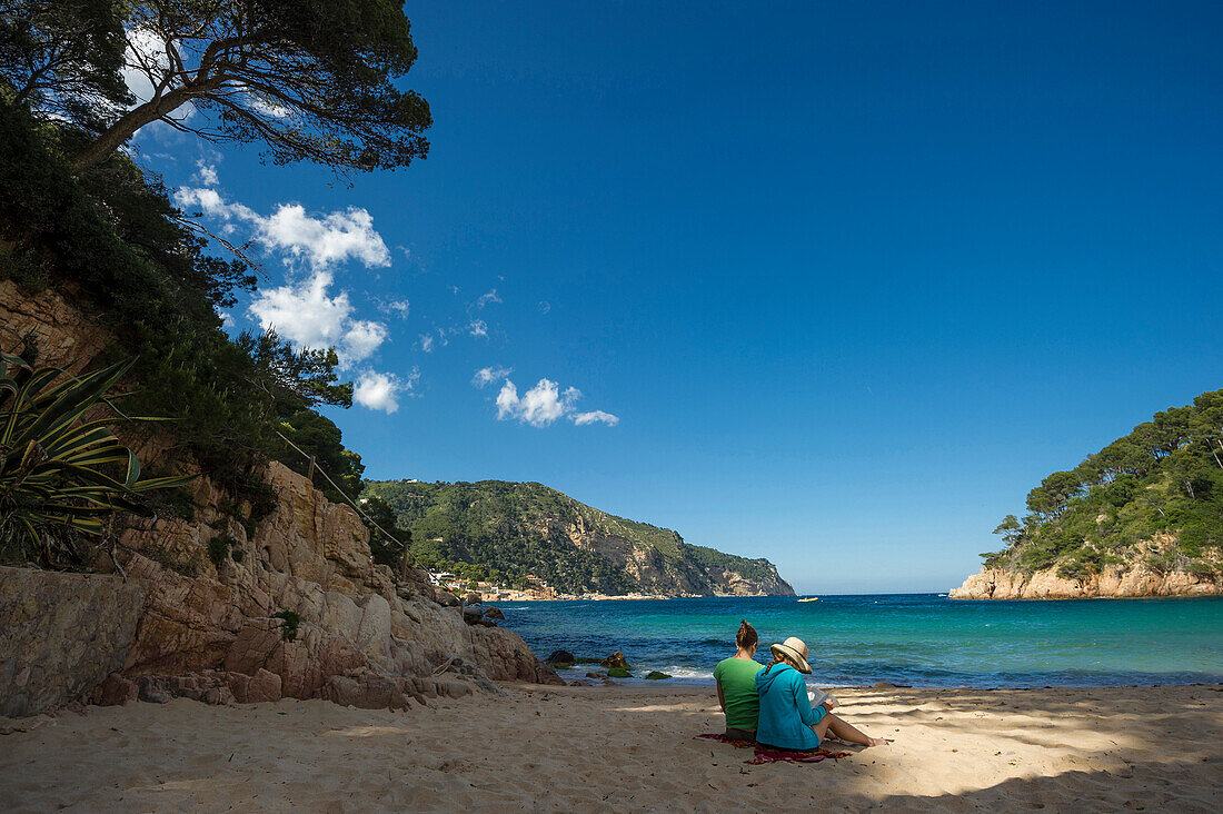 Two women reading a book on the beach, Aiguablava, near Begur, Costa Brava, Spain