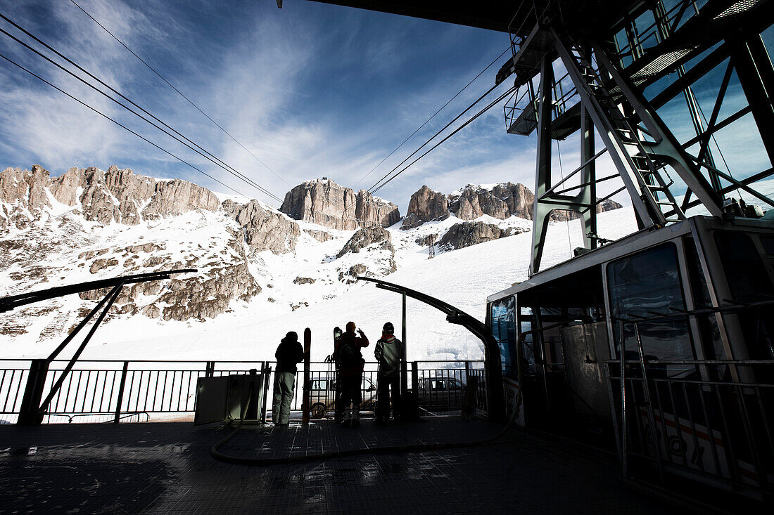 Three skiers standing in gondola lift valley station, Marmolata, Trentino, Italy