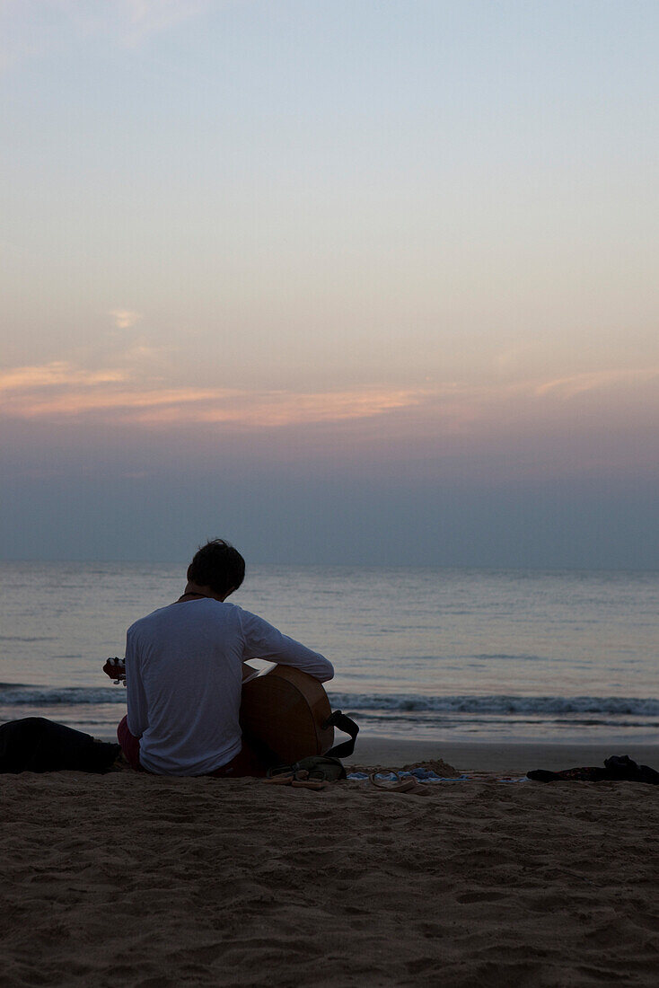 Tourist spielt Gitarre am Strand bei Sonnenuntergang, Agonda, Goa, Indien