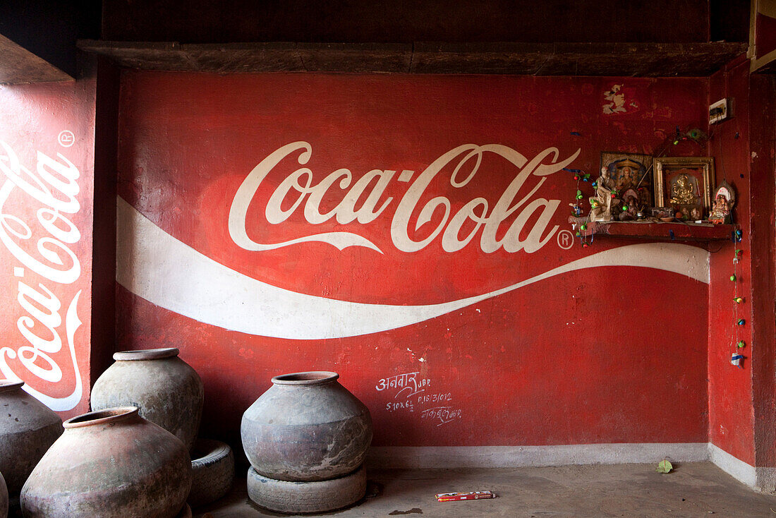 Trinkwasserbehälter und Kontrast zwischen modernem Cola Schriftzug und Hausaltar in einem Restaurant, Khajuraho, Madhya Pradesh, Indien