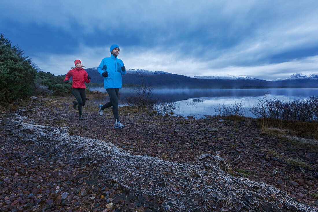 Young couple jogging along Loch Maree, Northwest Highlands in background, Scotland, United Kingdom
