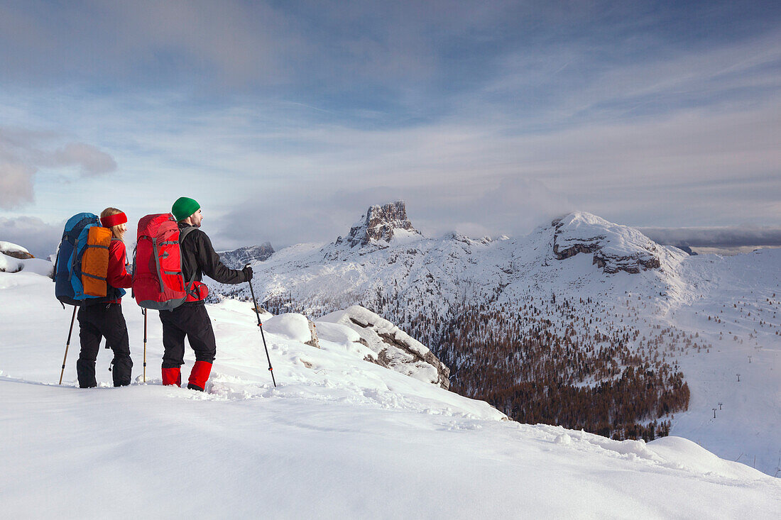 Junges Paar mit Rucksäcken im Schnee betrachtet Aussicht, Naturpark Fanes-Sennes-Prags, Tal des Passo di Falzarego, Dolomiten, Belluno, Venetien, Italien