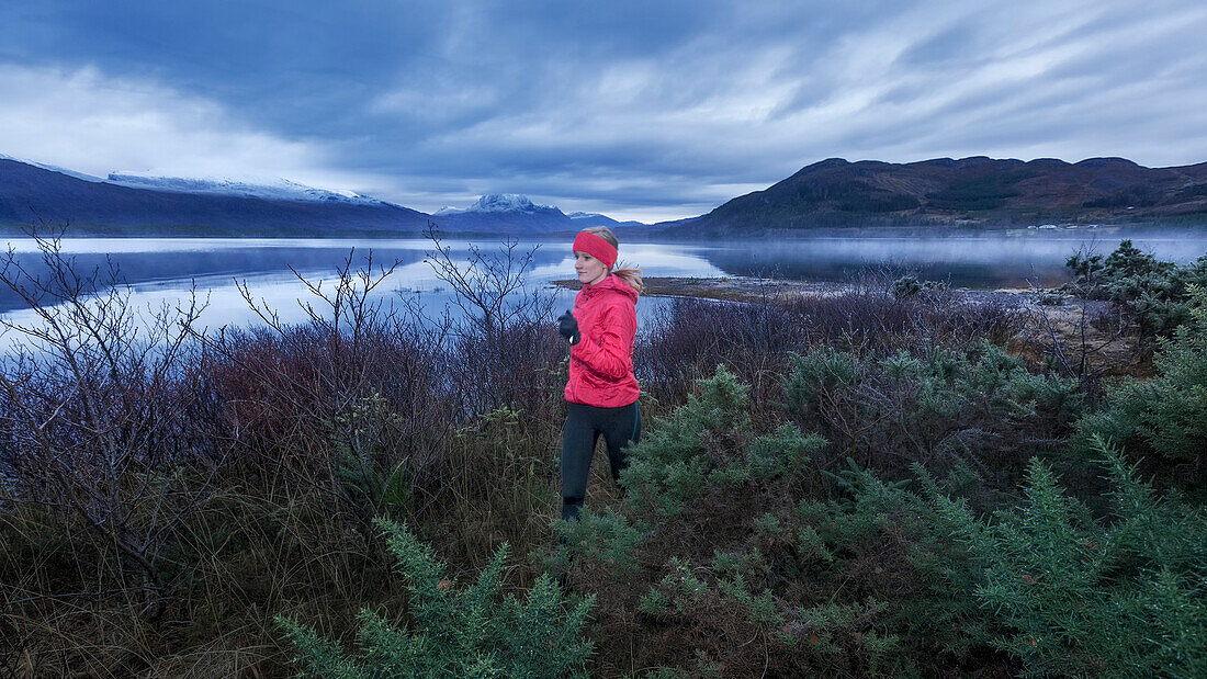 Young woman jogging along Loch Maree, Northwest Highlands in the background, Scotland, United Kingdom