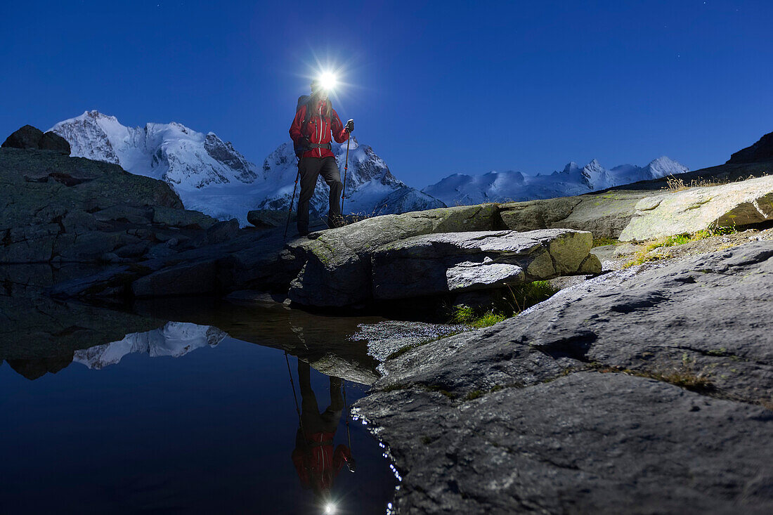 Junge Frau mit Stirnlampe wandert an einem Bergsee oberhalb des Rosegtales, Piz Morteratsch, Piz Bernina und Piz Roseg im Hintergrund, Engadin, Kanton Graubünden, Schweiz
