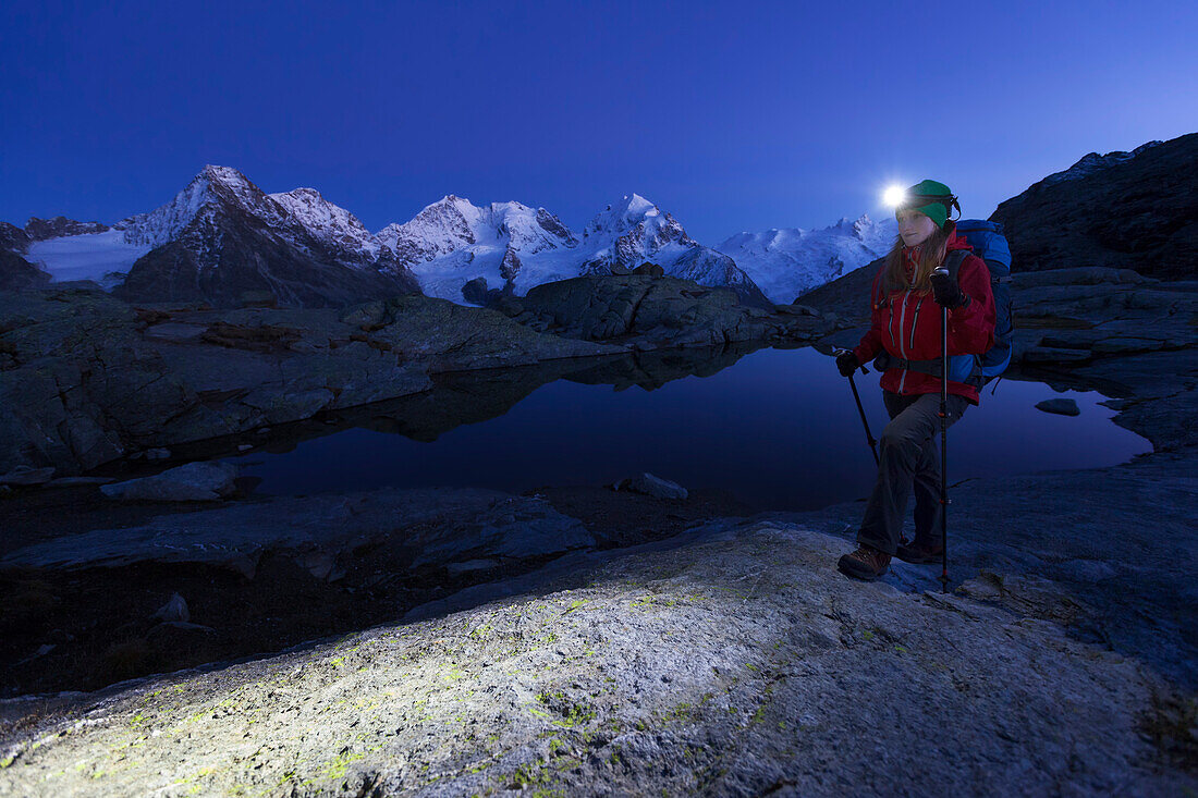 Junge Frau mit Stirnlampe wandert an einem Bergsee oberhalb des Rosegtales, Piz Morteratsch, Piz Bernina und Piz Roseg im Hintergrund, Engadin, Kanton Graubünden, Schweiz