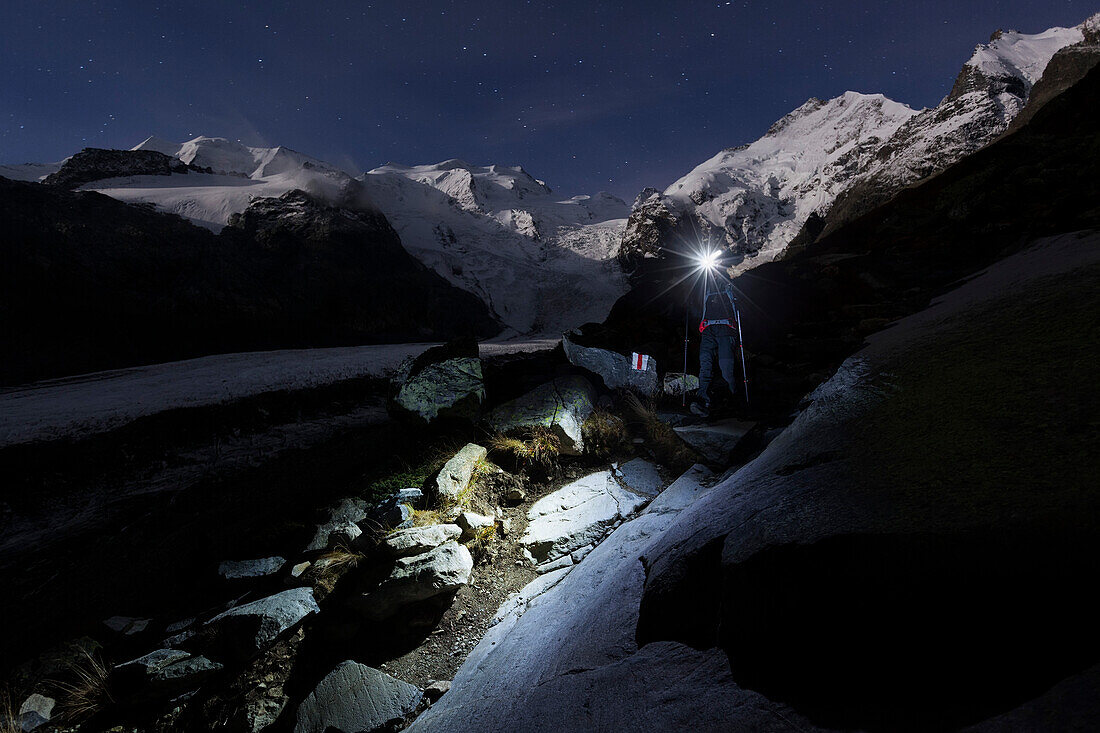 Hiker with headlamp in Morteratsch valley, Piz Palu, Piz Bernina and Piz Zupo in background, Engadin, Canton of Grisons, Switzerland