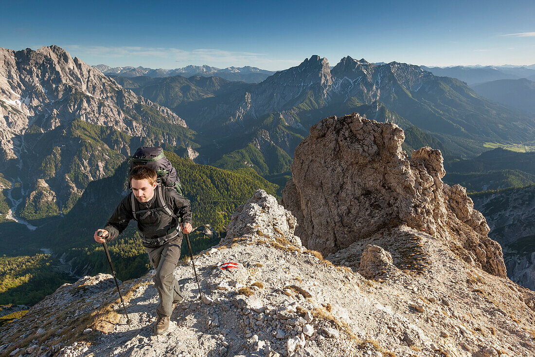 Junger Mann mit Rucksack wandert auf einem steilen Bergpfad am Großen Buchstein, Nationalpark Gesäuse, Hochtor und Admonter Reichensteingruppe im Hintergrund, Ennstaler Alpen, Steiermark, Österreich