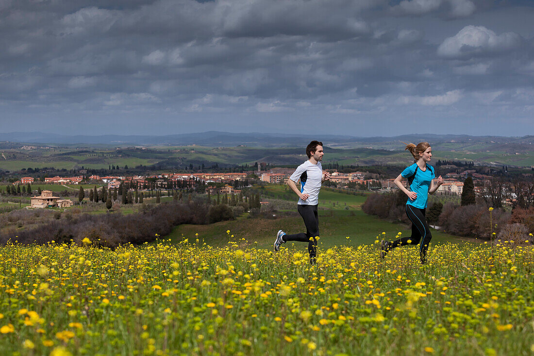 Young couple jogging along a blooming flower meadow, San Quirico d Orcia, Tuscany, Italy