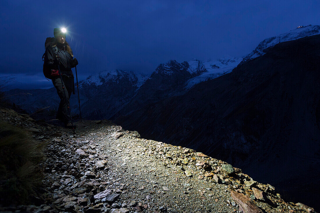 Young woman with headlamp hiking in twilight, Ortler in the background, Stelvio National Park, South Tyrol, Italy