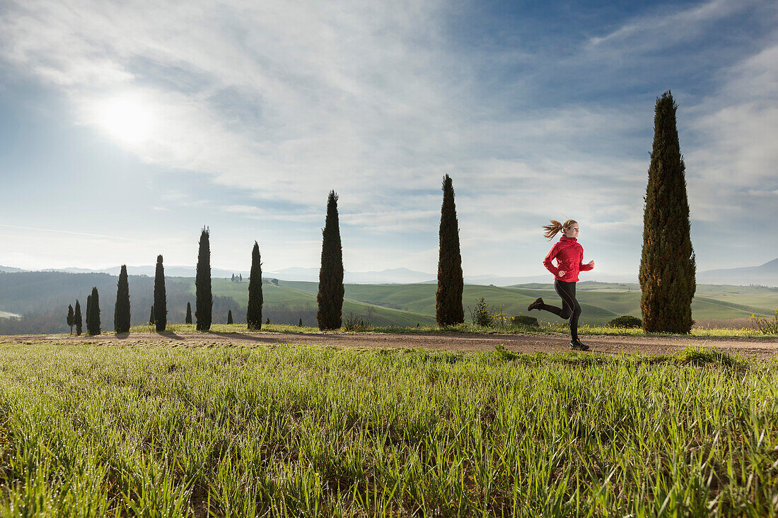 Junge Frau joggt über einen Weg mit Zypressen, Toskana, Italien