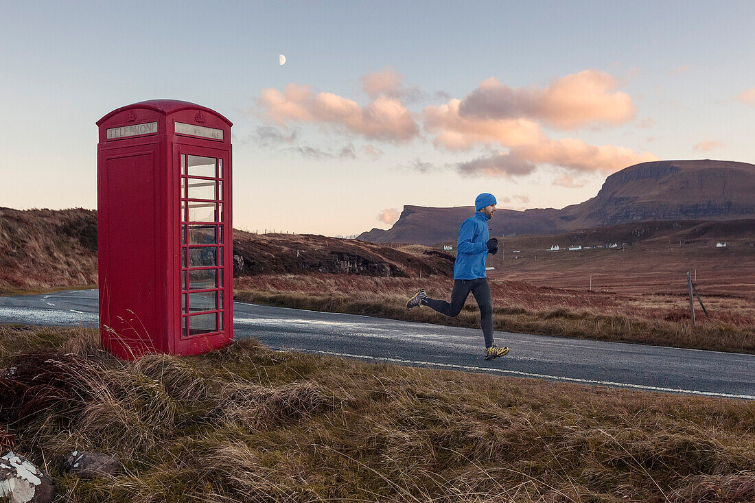 Young man jogging, passing a red booth, Isle of Skye, Trotternish Peninsula, Scotland, United Kingdom