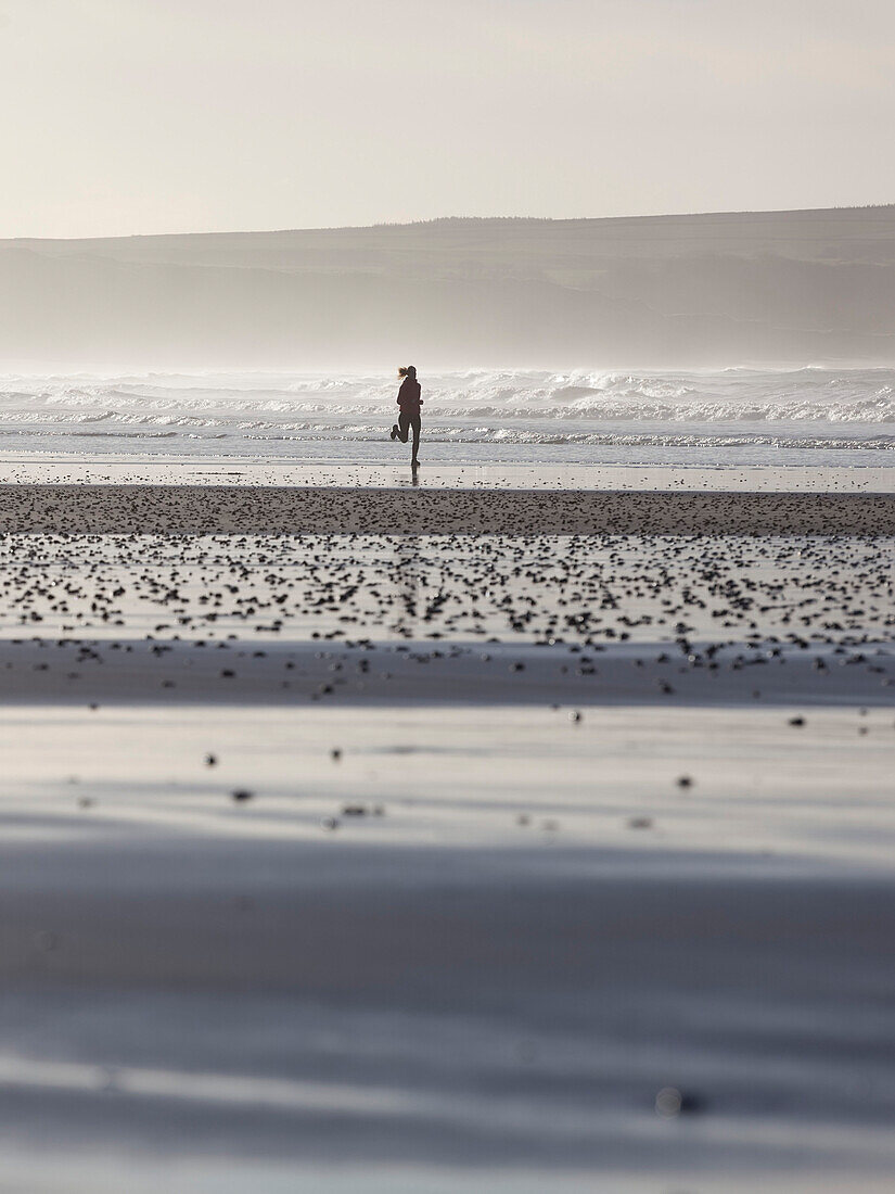 Junge Frau joggt am Strand im Gegenlicht, Dunnet Bay, Caithness, Schottland, Großbritannien