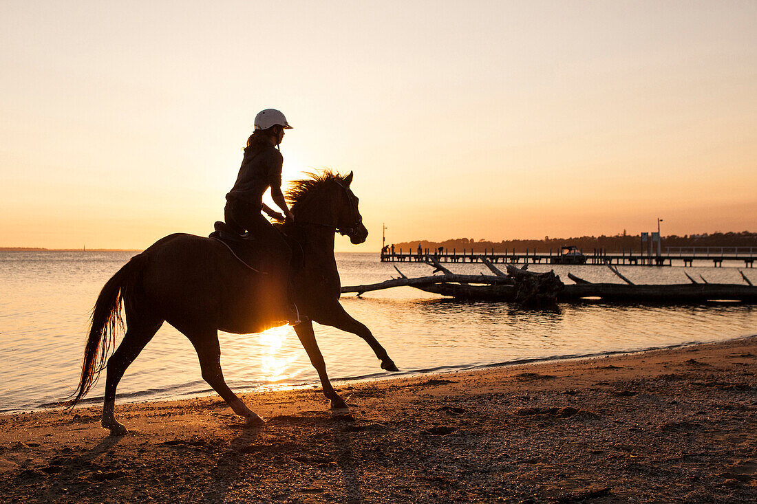 Mädchen reitet im Sonnenuntergang am Lake King, Metung, Victoria, Australien