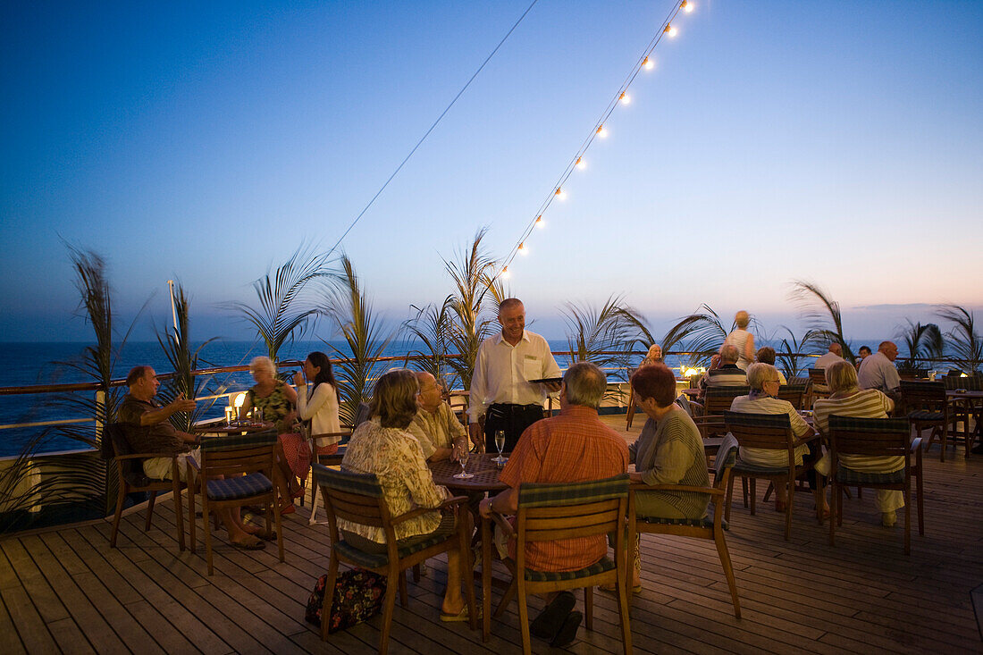 Passengers enjoying drinks on the deck of cruise ship MS Delphin (Passat Kreuzfahrten) at dusk, Caribbean Sea