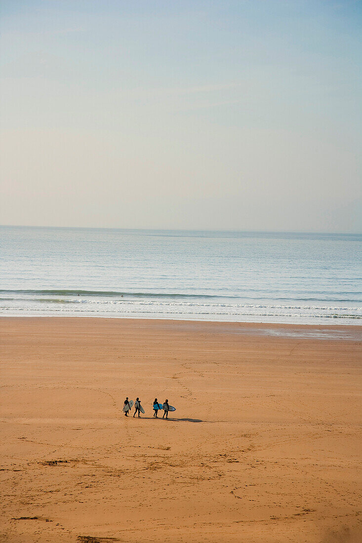 Group Of Surfers Walking On The Beach With Their Boards Towards The Sea In Putsborough Sands, North Devon, Uk