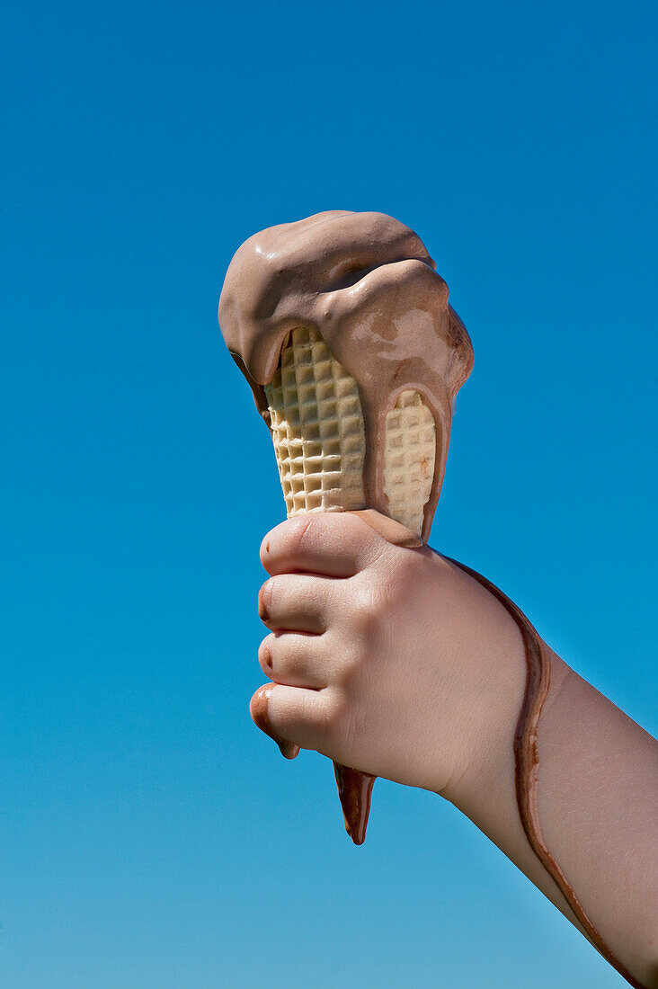 Girl Holding A Melting Ice Cream Against A Blue Sky, West Sussex, Uk