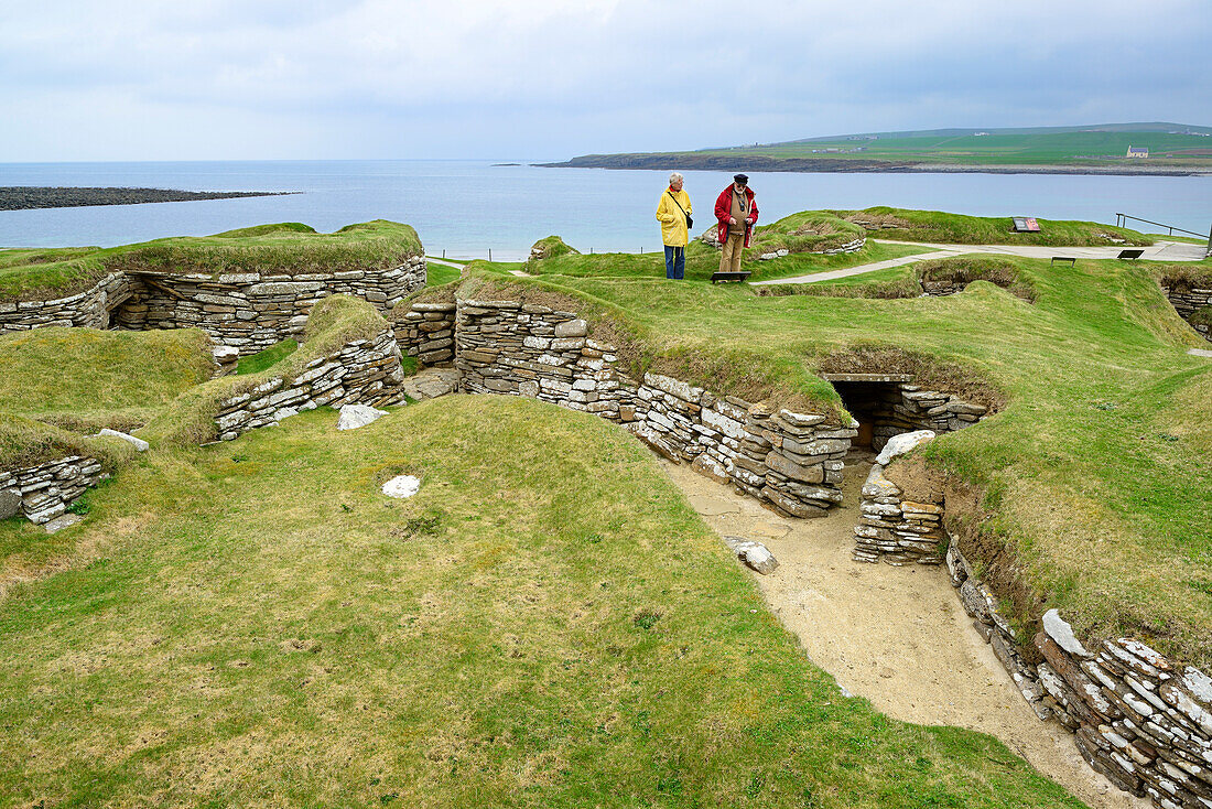 Zwei Personen besichtigen die steinzeitliche Siedlung Skara Brae, Skara Brae, UNESCO Weltkulturerbe The Heart of Neolithic Orkney, Orkney Inseln, Schottland, Großbritannien, Vereinigtes Königreich