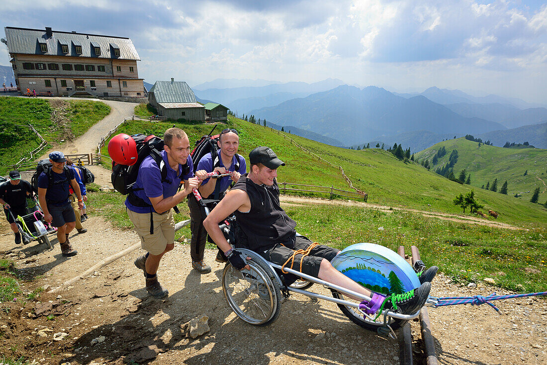 Gruppe von Wanderern begleitet Mann im Rollstuhl, Rotwandhaus im Hintergrund, Bergtour mit Behinderten, Rotwand, Spitzing, Bayerische Alpen, Oberbayern, Bayern, Deutschland