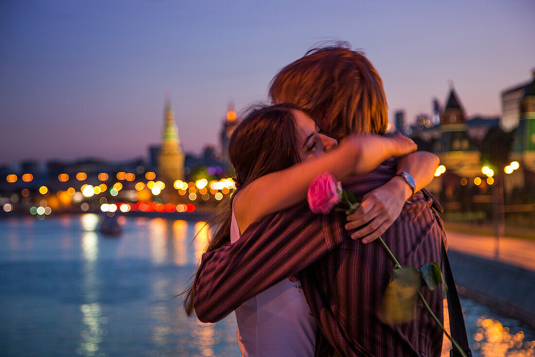 Young couple embracing on a bridge across the Moskva river with illuminated Kremlin buildings in the background, Moscow, Russia, Europe