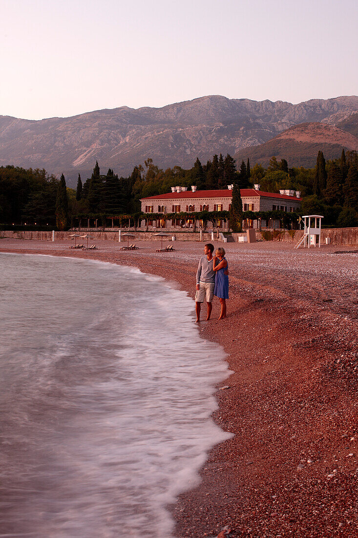 Couple at beach in evening light, Villa Milocer in background, Aman Sveti Stefan, Sveti Stefan, Budva, Montenegro