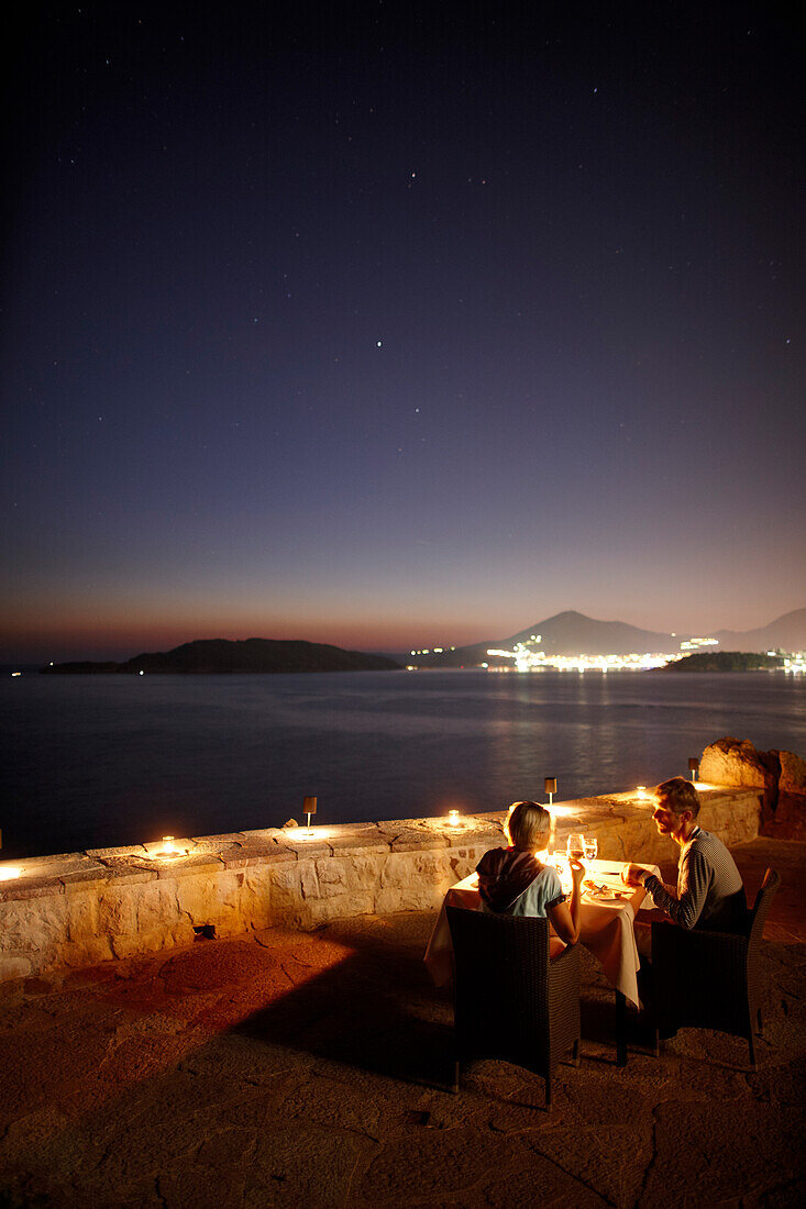 Paar beim Abendessen auf der Terrasse des Queen's Chair Restaurant, Blick auf Budva Bucht, Aman Sveti Stefan, Sveti Stefan, Budva, Montenegro