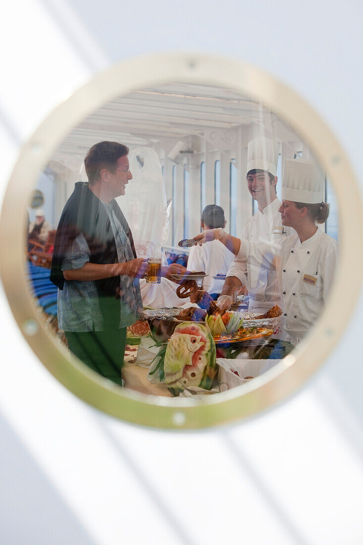 Blick auf Köche und Passagier durch ein Bugfenster von Kreuzfahrtschiff MS Deutschland (Reederei Peter Deilmann) während des traditionellen Frühschoppens auf See, Südpazifik, nahe Chile, Südamerika