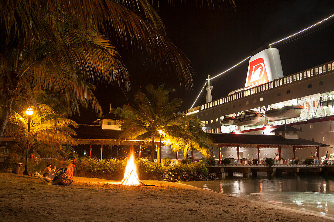 Strandparty mit Lagerfeuer direkt vor Kreuzfahrtschiff MS Deutschland (Reederei Peter Deilmann) an der Pier bei Nacht, Port Antonio, Portland, Jamaika, Karibik